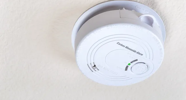 White carbon monoxide alarm mounted on a textured ceiling with indicator light and test button.