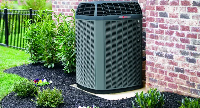 Outdoor HVAC unit installed next to brick house with landscaped garden and black mulch.