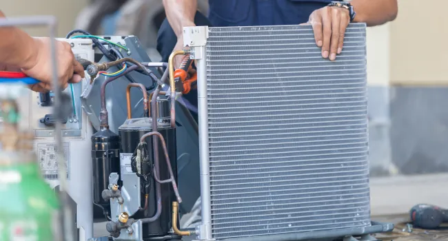 Technician repairing an air conditioning unit with tools on a concrete floor, focusing on condenser and wiring.