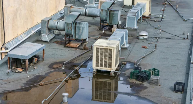 Rooftop with HVAC units, ductwork, and puddles of water reflecting the equipment on a flat building roof.