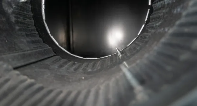 Close-up interior view of a dark ribbed metal pipe with screws inside, showing texture and depth.