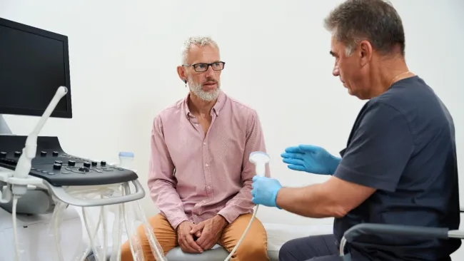 Doctor explaining ultrasound procedure to mature male patient in medical examination room