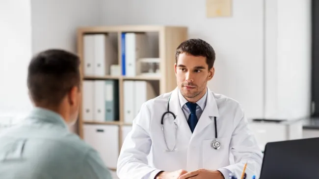 Male doctor attentively listening to patient during consultation in a modern medical office.