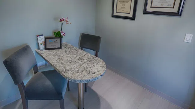 Modern office corner with marble table, gray chairs, orchid plant, and framed certificates on blue walls