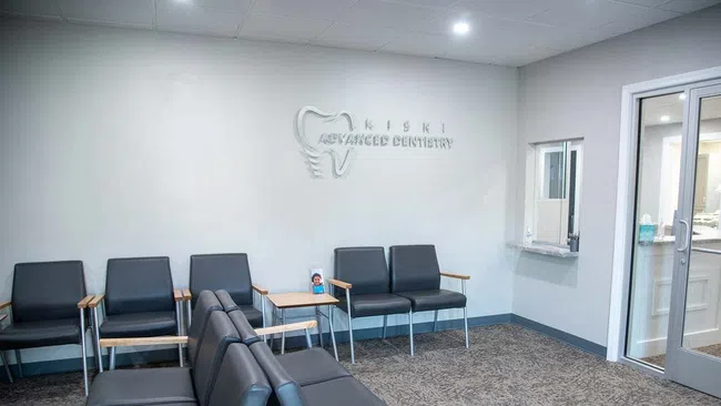 Modern dental office waiting room with black chairs, wooden armrests, and Kisiki Advanced Dentistry logo on wall.