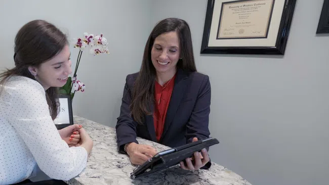 Two women sitting at a marble table discussing information on a tablet in a professional office setting