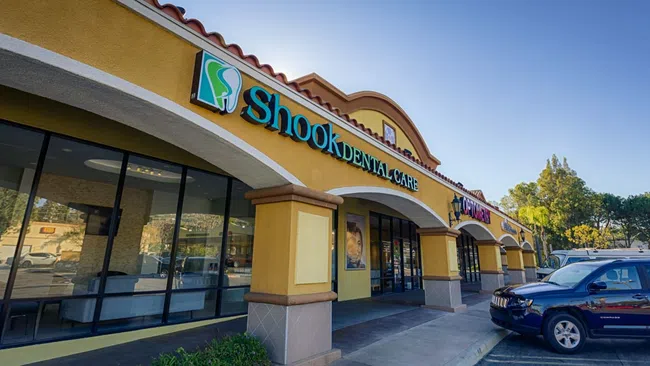 Exterior view of Shook Dental Care with clear signage on a sunny day and parked vehicles outside.
