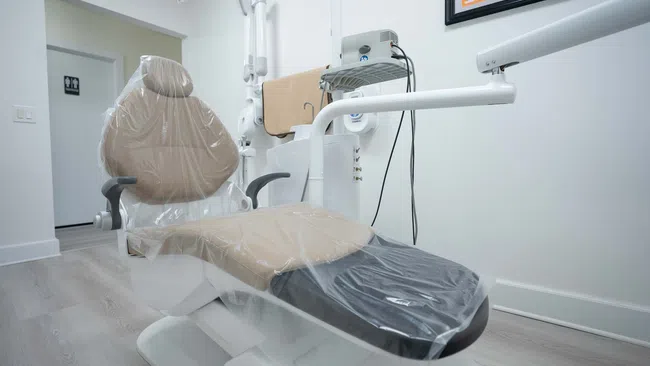 Modern dental chair covered in protective plastic inside a clean, bright dental clinic room.