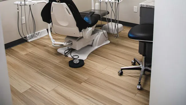Modern dental office with a patient chair, dental equipment, wooden flooring, and soft wall artworks.