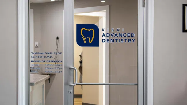 Glass door entrance of Kiski Advanced Dentistry with office hours and dental logo visible.