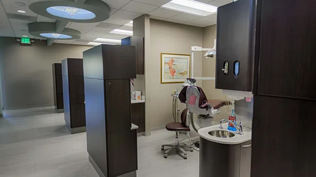 Modern dental clinic interior with treatment chairs, dark wood cabinetry, and bright overhead lighting.