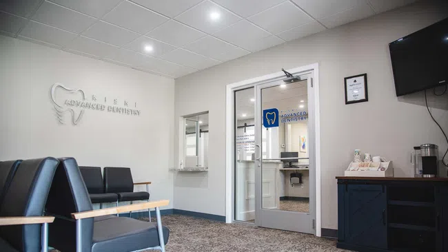 Modern dental office waiting room with black chairs, beige walls, reception window, and door to dentist's office.