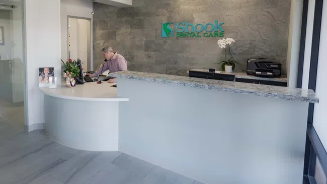 Modern dental clinic reception with a curved desk, granite countertop, and man working at computer.