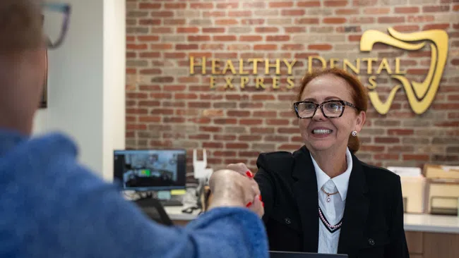 Receptionist in black blazer shaking hands with patient at Healthy Dental Express front desk