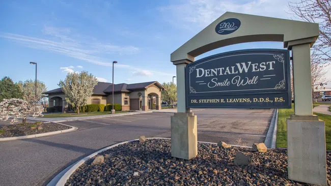 DentalWest clinic sign and building with landscaped parking lot and clear blue sky in daytime