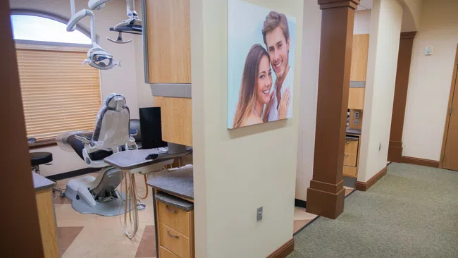 Interior of a modern dental office with a dental chair, cabinetry, and a hallway with a smiling couple photo.