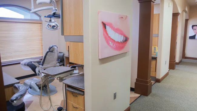Modern dental clinic room with dental chair, equipment, and smiling teeth wall art in a clean hallway.