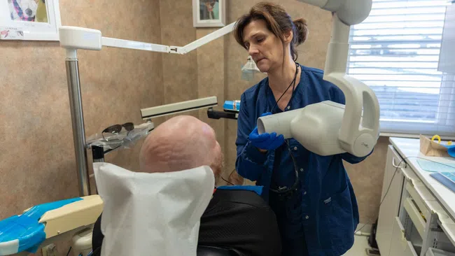 Dental professional using X-ray machine to examine elderly male patient's teeth in dental clinic