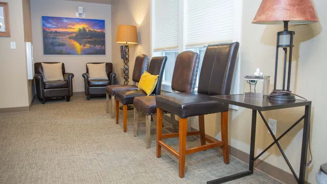 Well-lit waiting room with leather chairs, side tables, lamps, and a sunset landscape painting on the wall.