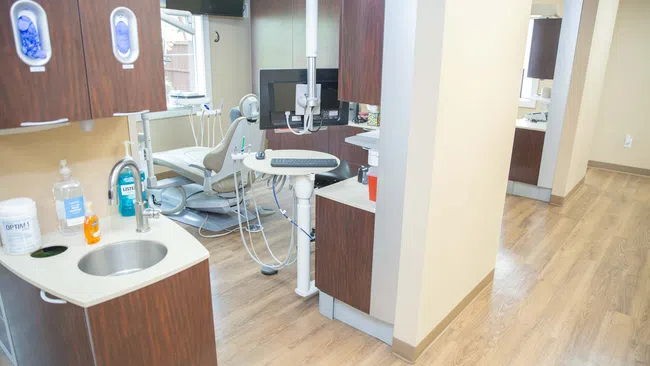 Bright modern dental clinic with wooden floors, dental chair, sink, and cabinetry in treatment area.
