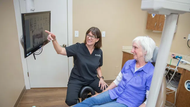 Dentist explaining dental X-rays to a senior woman patient seated in a dental chair in a clinic room.
