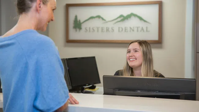 Dental receptionist smiling and assisting a patient at the Sisters Dental office front desk.