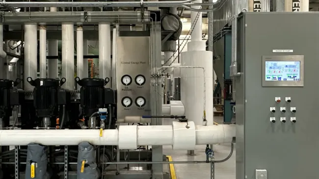 Industrial energy plant with control panels, pipes, gauges, pumps, and labeled feed water system indoors