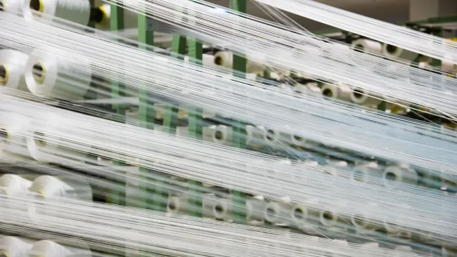 Industrial textile machine with multiple spools of white thread stretched and aligned in a factory setting.
