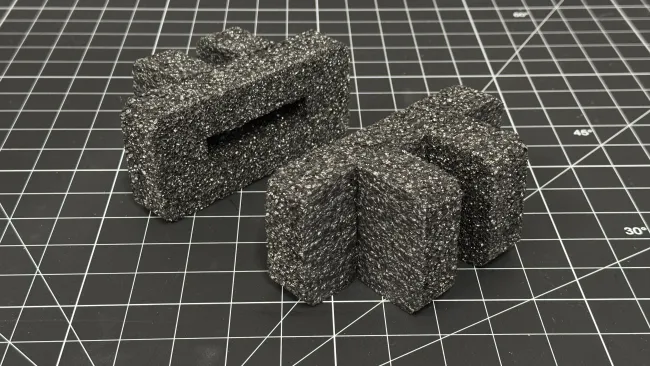 Two black textured foam pieces with rectangular and curved shapes on a black cutting mat with measurement grid.