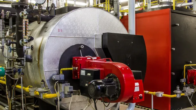 Industrial boiler system with red fuel burner, pressure gauges, pipes, and control valves in a factory setting