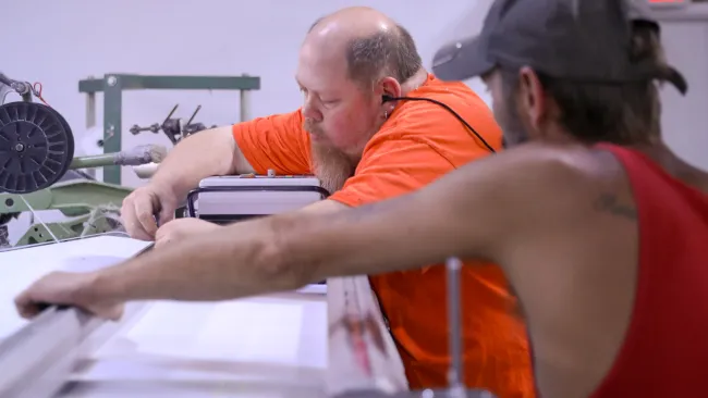Two men working together on a machine in an industrial workshop setting focused on precision tasks.