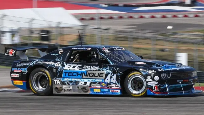 Black and blue race car number 44 speeding on a curved racetrack with red and white barriers in the background