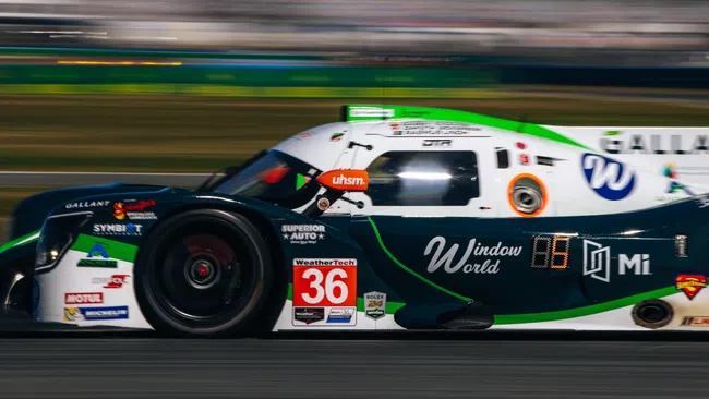 Green and white race car number 36 speeding on a track during a race event with motion blur background.