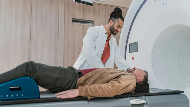 Doctor preparing middle-aged man for MRI scan in modern medical imaging room with large scanner.
