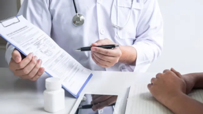 Doctor explaining medical information on clipboard to patient with tablet and medicine bottle on table