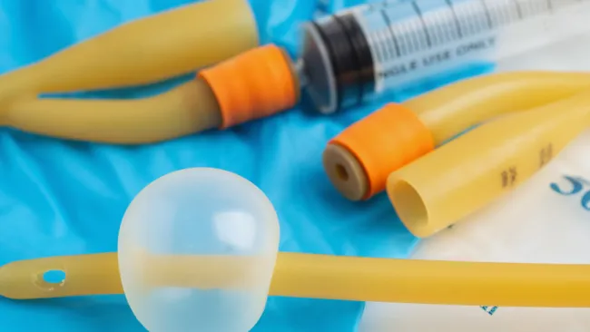 Medical catheter with balloon and syringe on blue medical gloves, close-up view of sterile equipment.