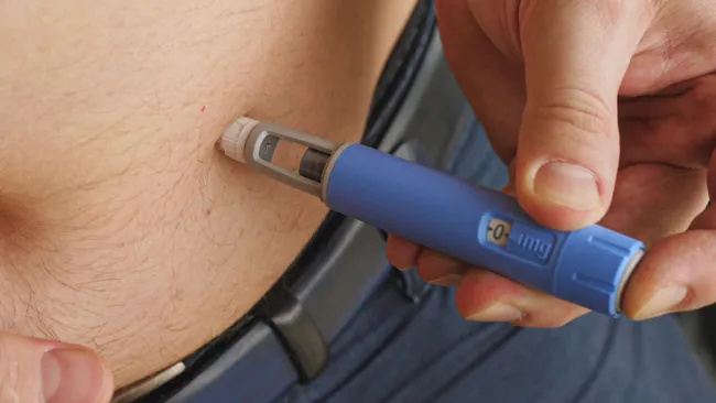 Person administering insulin injection using an insulin pen on abdominal area for diabetes management.