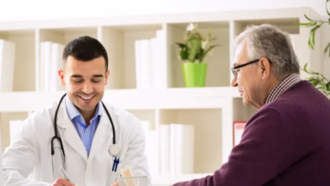 Doctor in white coat consulting and writing notes while senior male patient listens attentively in medical office