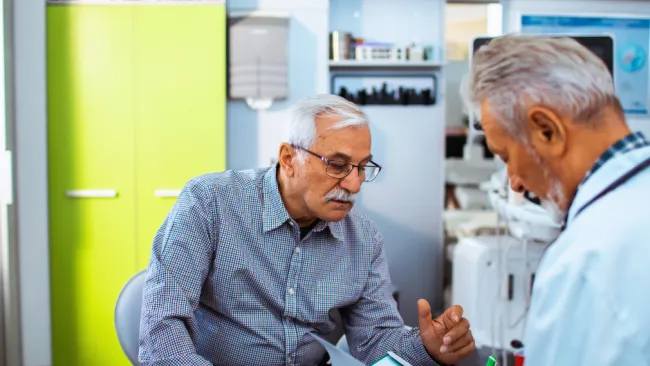 Senior man consulting with doctor in medical office discussing health documents together.