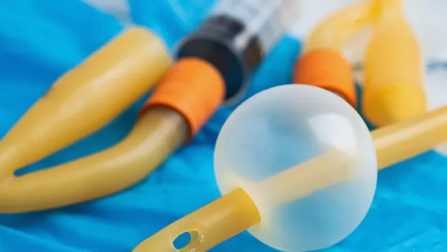 Close-up of medical urinary catheters with a balloon component on a blue medical glove background.