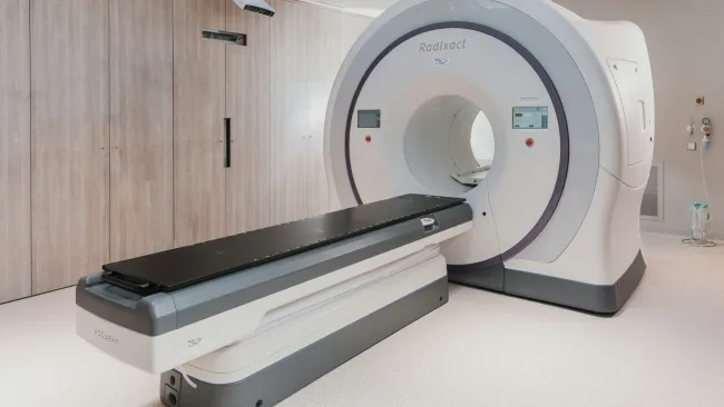 Modern Radixact CT scanner machine in a clean, well-lit medical imaging room with wood-paneled walls