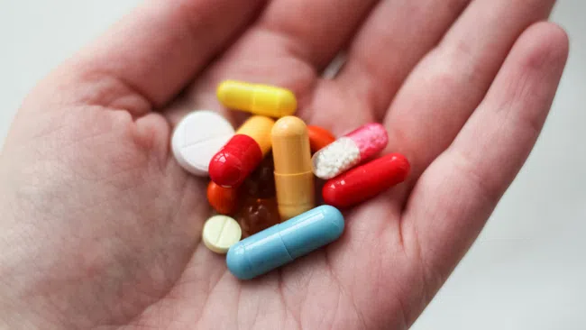 Hand holding various colorful capsules and tablets of medicine on a light background