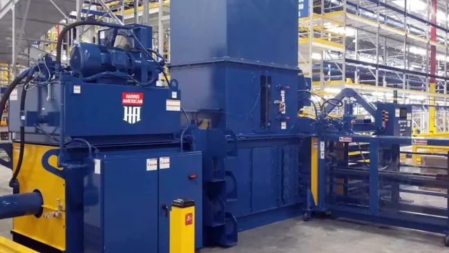Large blue and yellow industrial machine inside spacious warehouse with metal shelving and concrete floor.