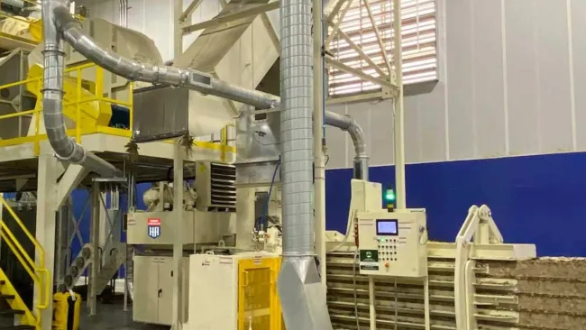 Industrial machinery with metal pipes and control panels processing large compressed blocks in a factory setting