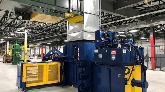Large industrial machine in a spacious factory with yellow and blue components under ceiling ducts and lighting