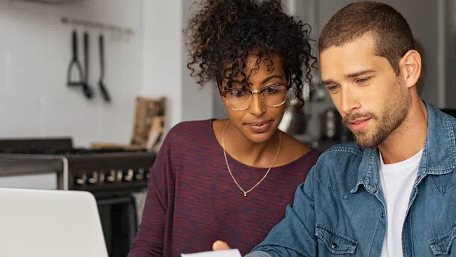 Couple reviewing receipts and finances together using a laptop at home in a modern kitchen setting.