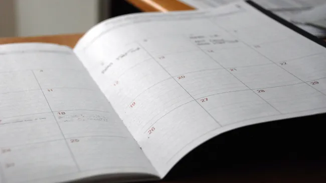 Open planner calendar on wooden desk showing monthly layout with dates and blank notes space.