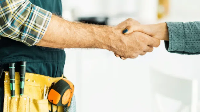 Contractor shaking hands with client, wearing tool belt and protective gloves in a bright room