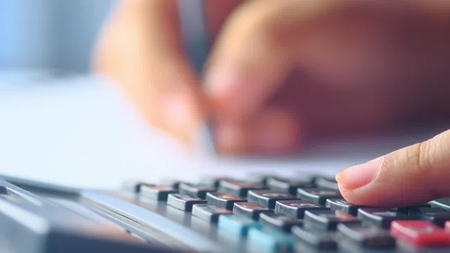 Person using a calculator while writing notes, focusing on financial calculations or budgeting tasks.