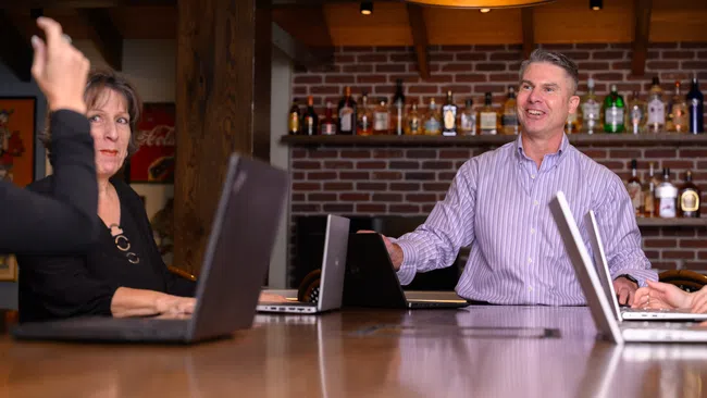 a couple of men sitting at a table with laptops
